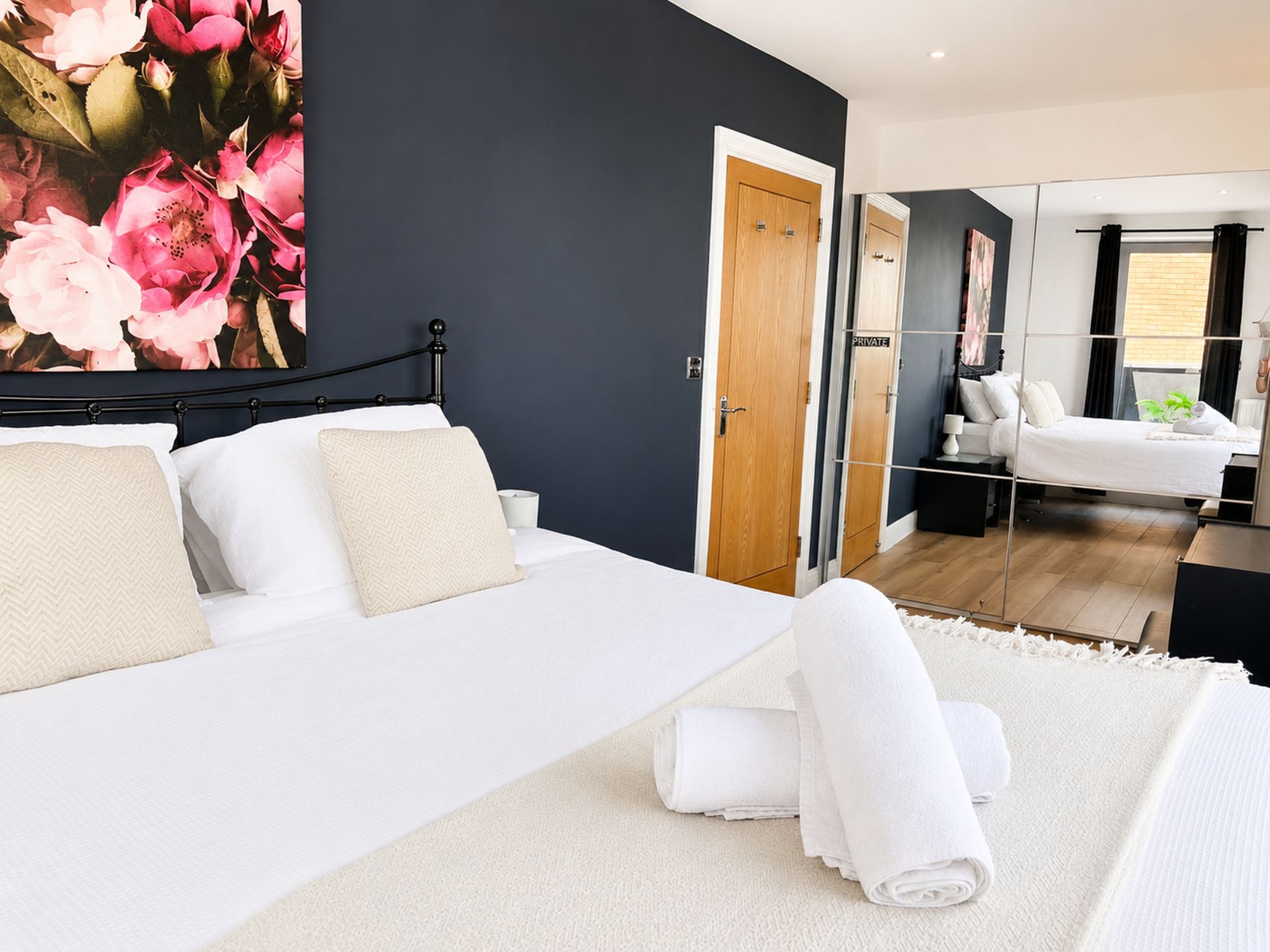 Un dormitorio moderno con cama, mesitas de noche, un espejo y una obra de arte floral grande en la pared.