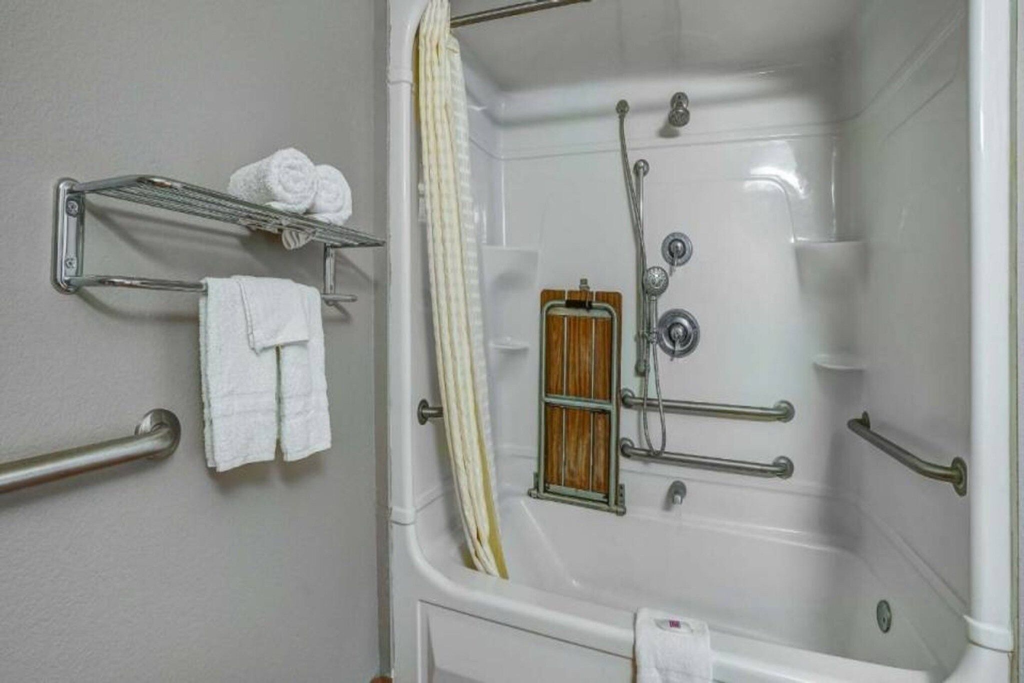 Une salle de bain équipée d’une baignoire, de barres d’appui, d’un rideau de douche et d’un porte-serviettes avec des serviettes.