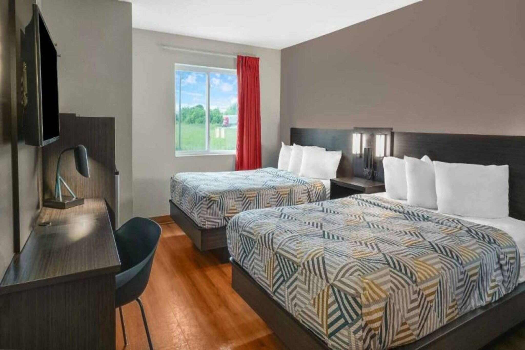 Une chambre d’hôtel avec deux lits, un bureau, une chaise, une télévision et une fenêtre donnant sur l’extérieur.