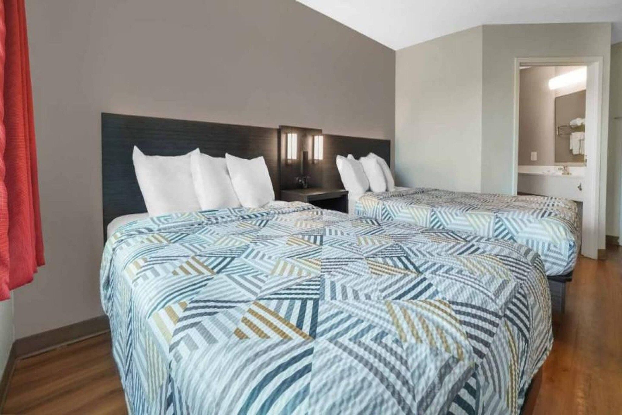 Habitación de hotel con dos camas, una mesita de noche y un baño visible a través de una puerta abierta.