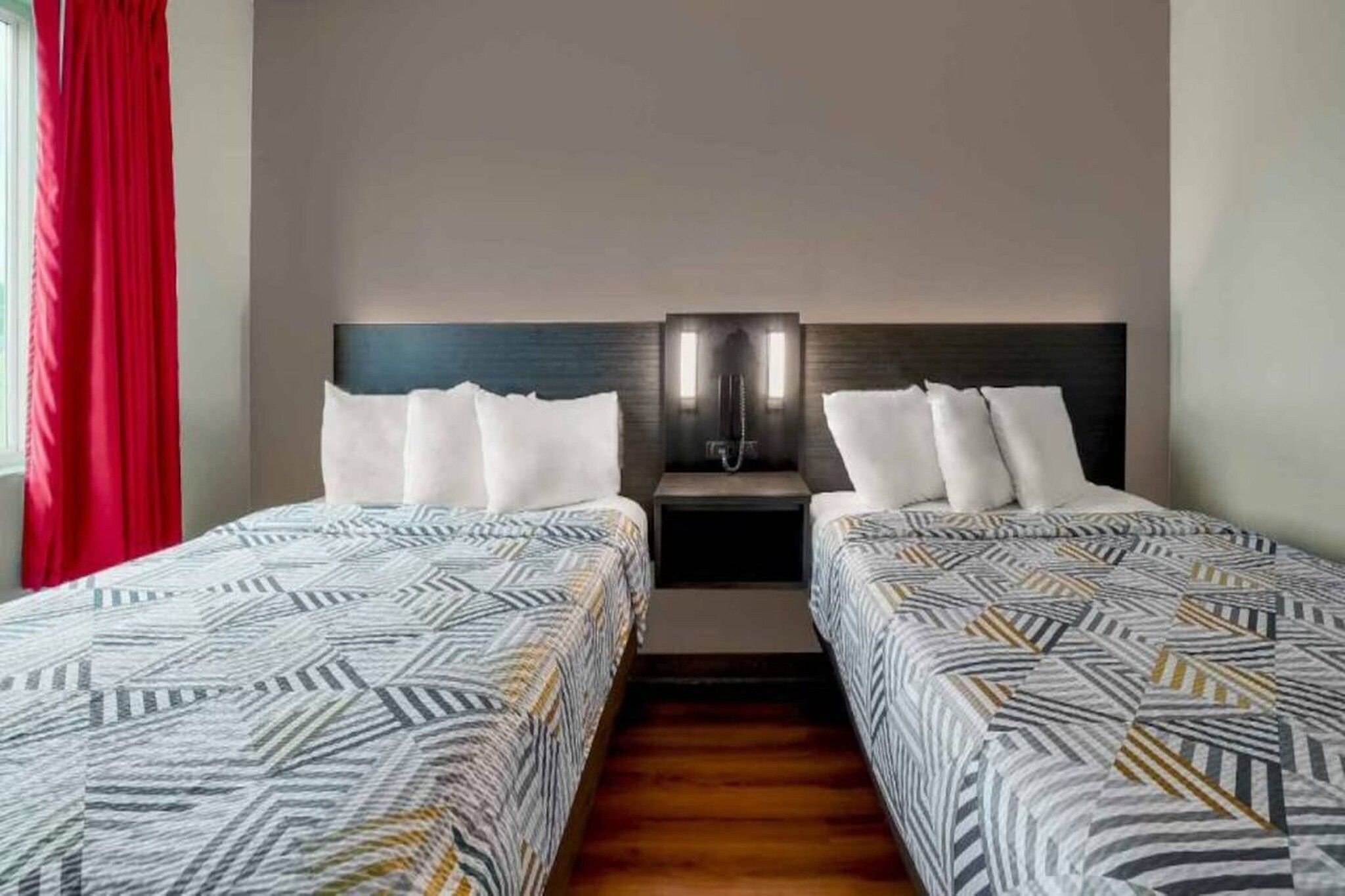 A hotel room with two beds, a nightstand, and a red curtain.