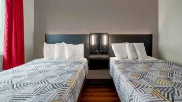 A hotel room with two beds, a nightstand, and a red curtain.