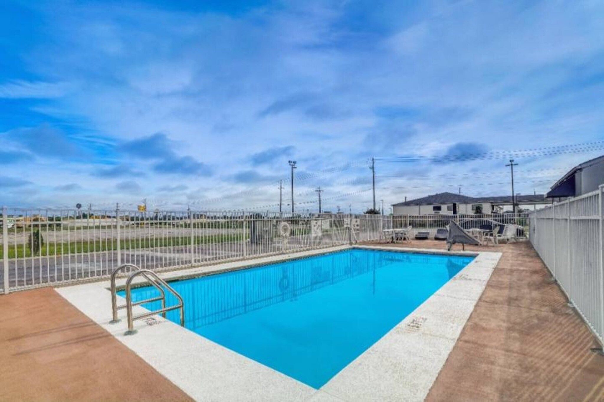 A rectangular swimming pool with a metal ladder, surrounded by a white fence, under a clear sky.