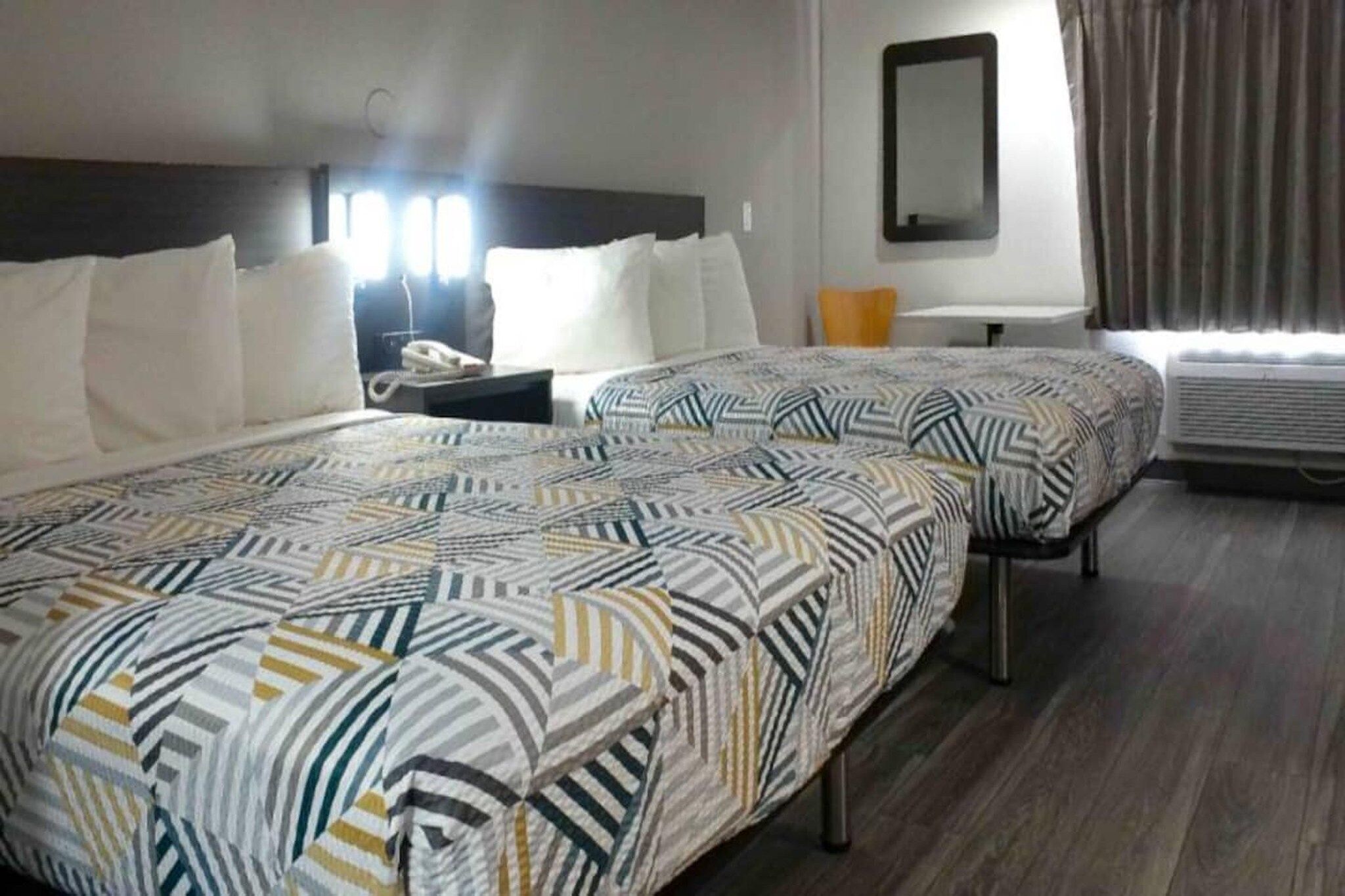 A hotel room with two beds, a nightstand, a mirror, and an air conditioning unit.