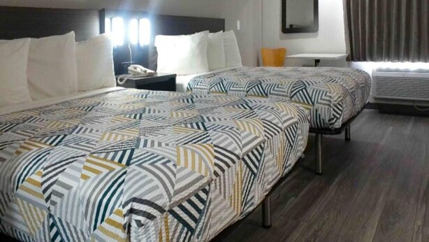 Een hotelkamer met twee bedden, een nachtkastje, een spiegel en een airconditioner.