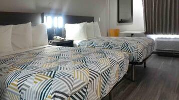 A hotel room with two beds, a nightstand, a mirror, and an air conditioning unit.