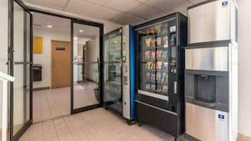 Un espace comprenant un distributeur automatique, un réfrigérateur et une porte donnant sur une autre pièce.