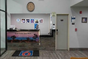 En reception med et ur, indrammede billeder, et skilt til værelse 66 og en reklameplakat for en mobil app.