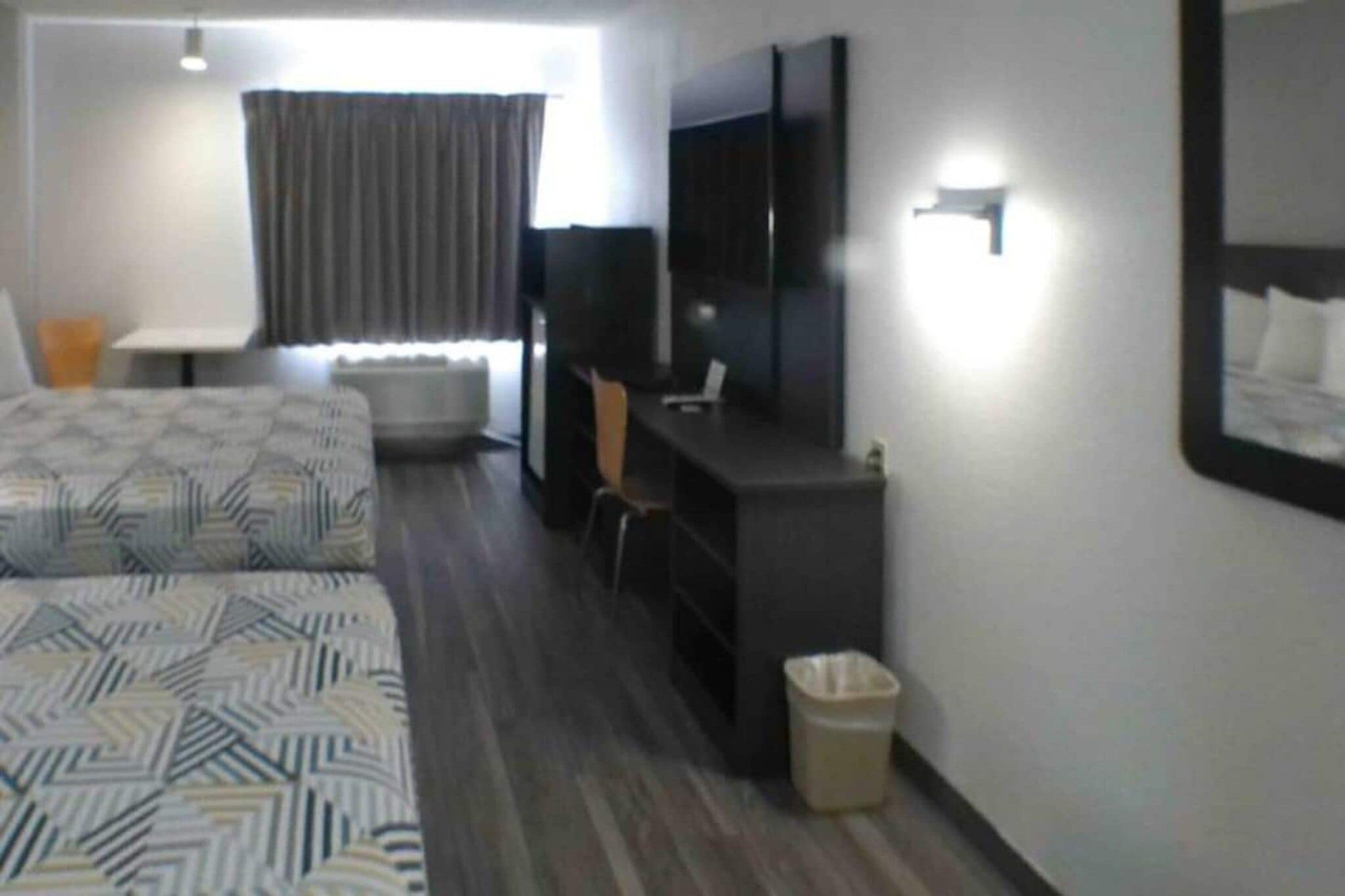 A hotel room with two beds, a desk, a chair, a TV, and a window with curtains.