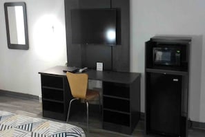 A room with a desk, chair, television, and a microwave.