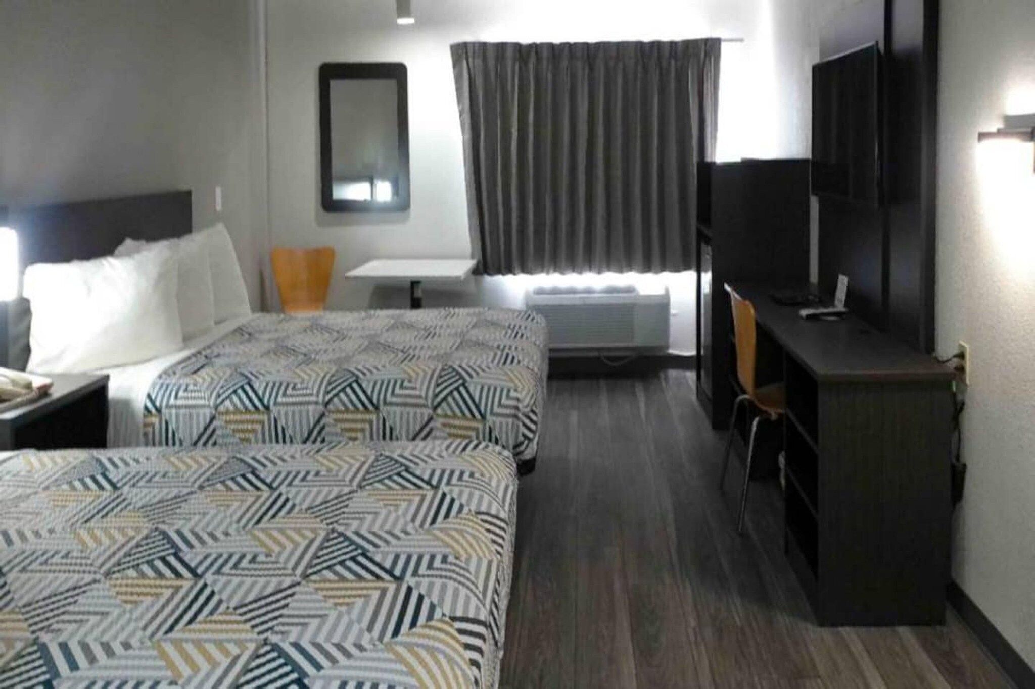 A hotel room with two beds, a desk, a chair, a television, and a window with curtains.