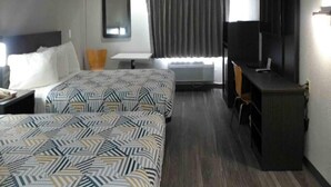 Een hotelkamer met twee bedden, een bureau, een stoel, een televisie en een raam met gordijnen.