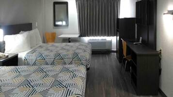 A hotel room with two beds, a desk, a chair, a television, and a window with curtains.
