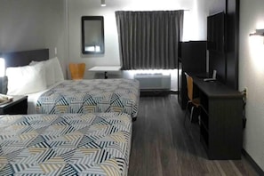 Et hotelværelse med to senge, et skrivebord, en stol, et fjernsyn og et vindue med gardiner.