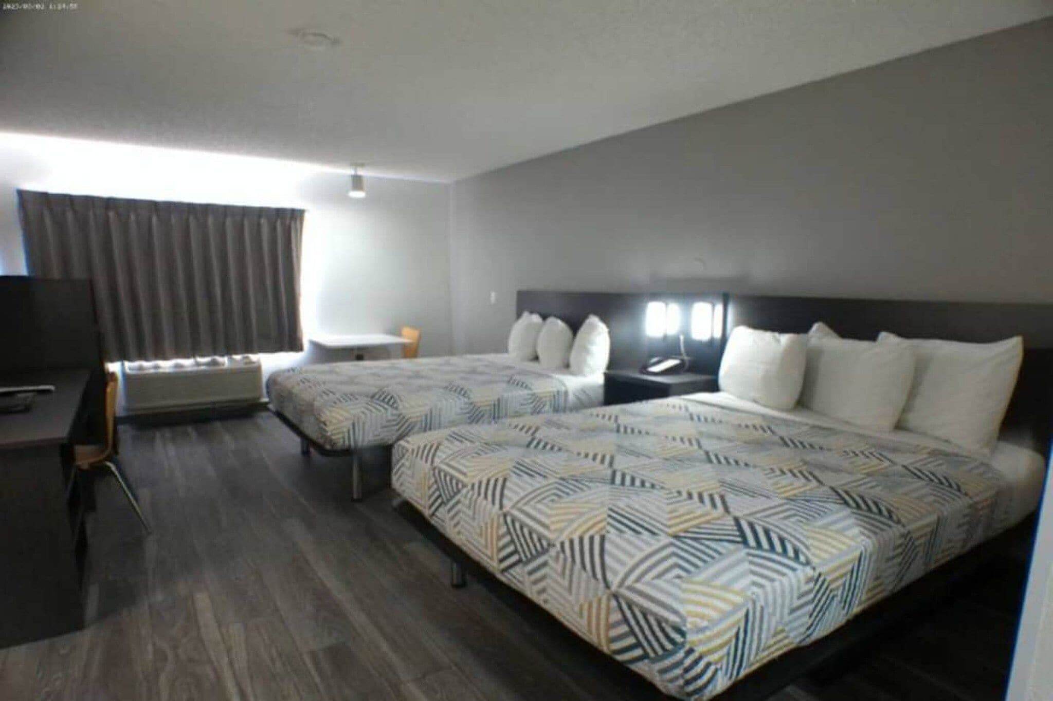 A hotel room with two beds, a desk, a chair, a TV, and a window with curtains.