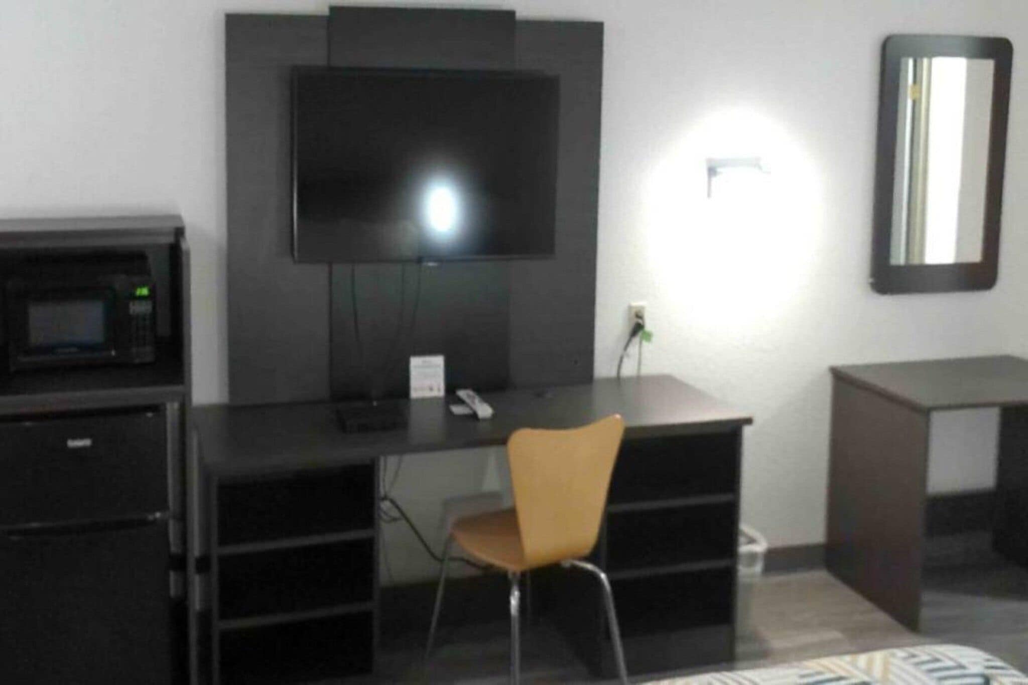 A room with a black desk, a television mounted on the wall, a microwave, and a chair.
