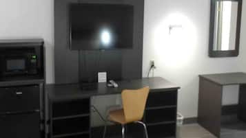 A room with a black desk, a television mounted on the wall, a microwave, and a chair.