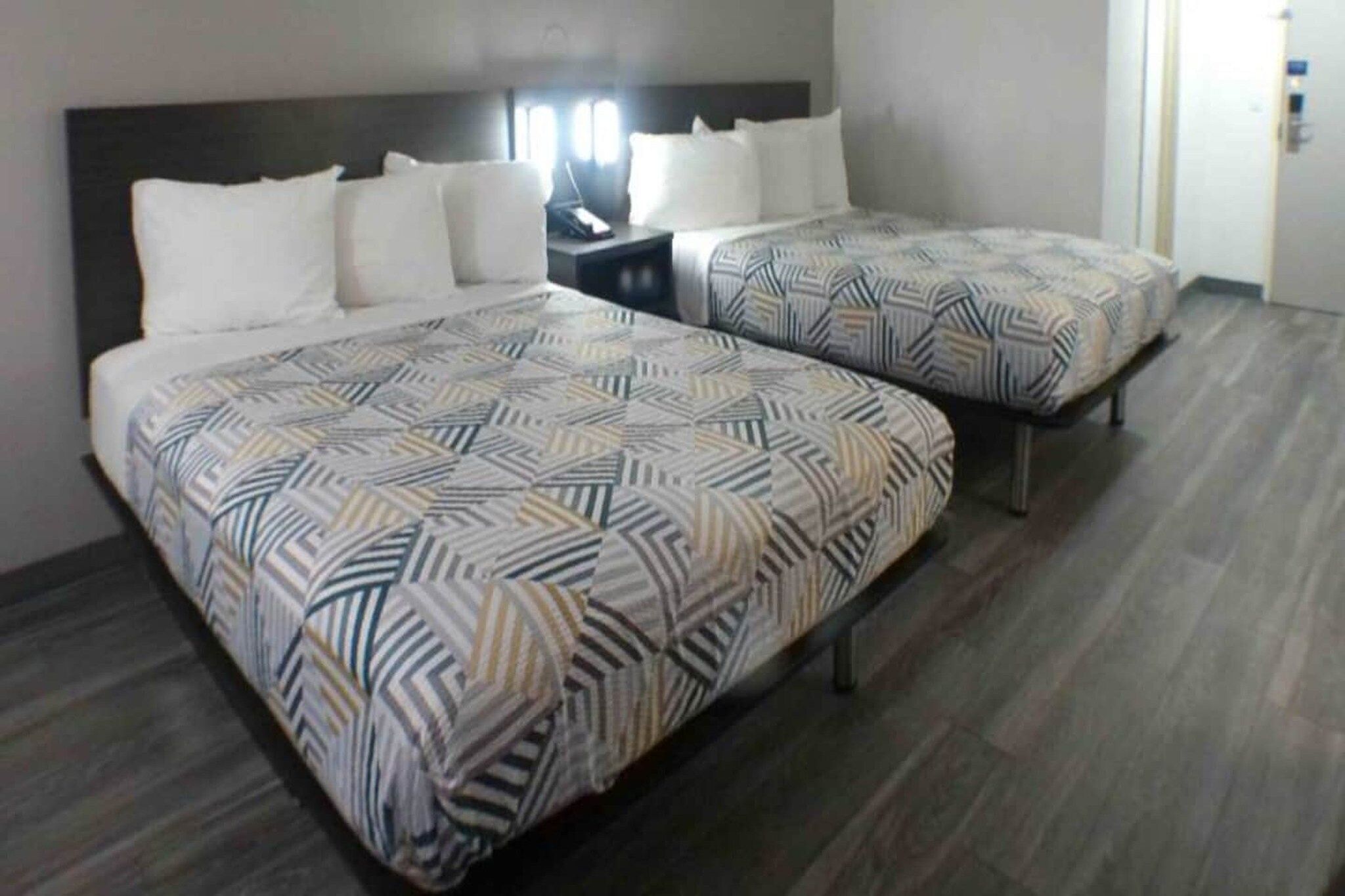 Habitación de hotel con dos camas, cada una con colcha estampada, una mesita de noche con lámpara y una puerta a la derecha.