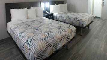 Habitación de hotel con dos camas, cada una con colcha estampada, una mesita de noche con lámpara y una puerta a la derecha.