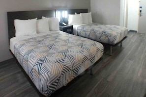 A hotel room with two beds, each with a patterned bedspread, a nightstand with a lamp, and a door to the right.