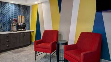 A hotel lobby with two red armchairs, a coffee machine, and a counter with a herringbone patterned wall.