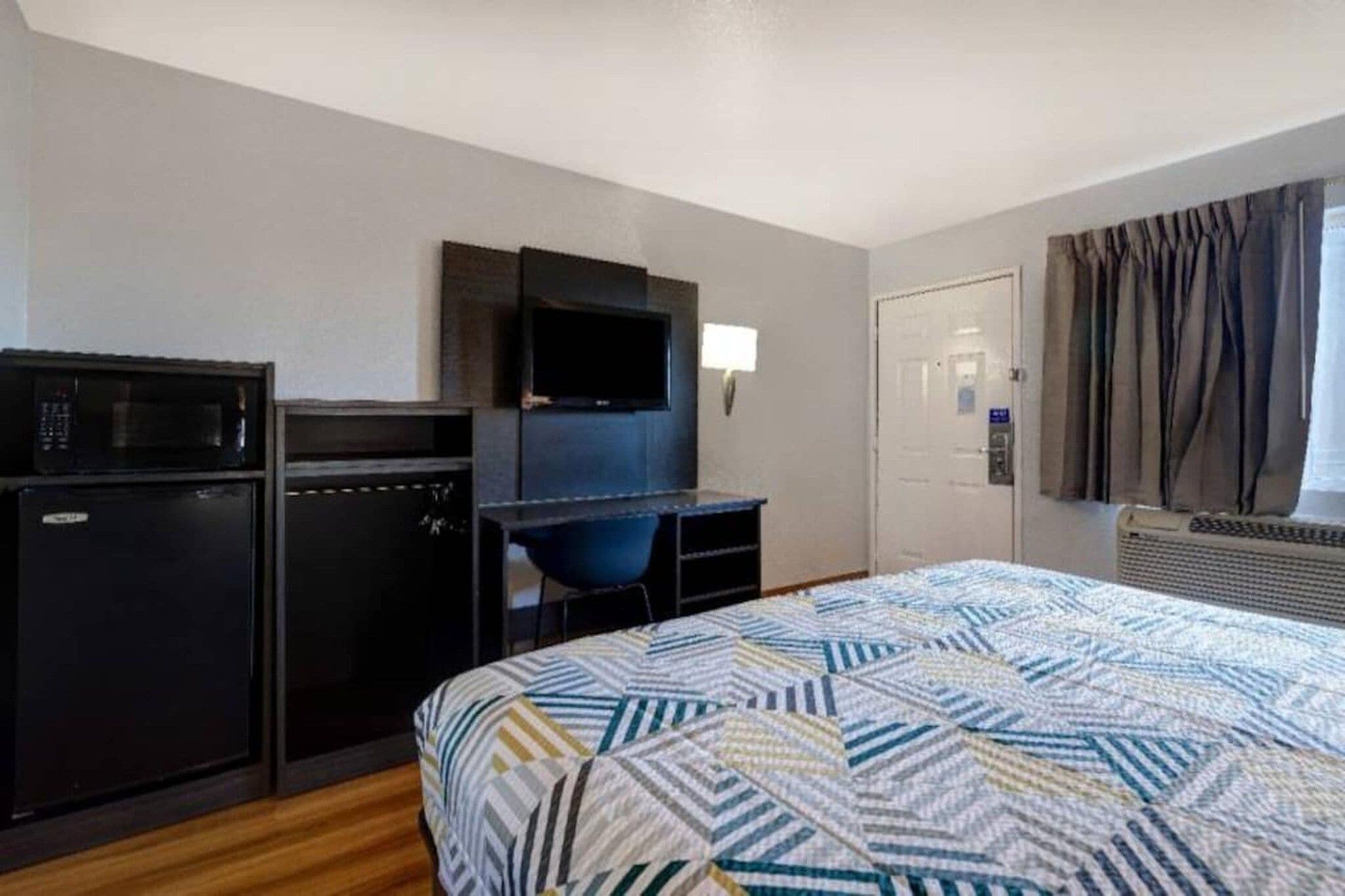 A hotel room with a bed, a desk with a television, a microwave, and a door.