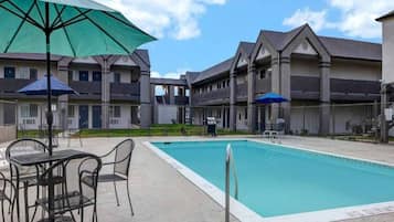 A swimming pool with a patio area, outdoor furniture, and a building with multiple balconies.