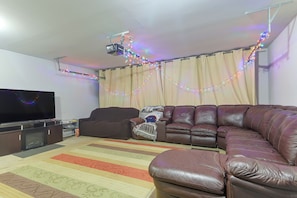 A living room with a leather sofa, a flat-screen TV, and a ceiling-mounted projector.