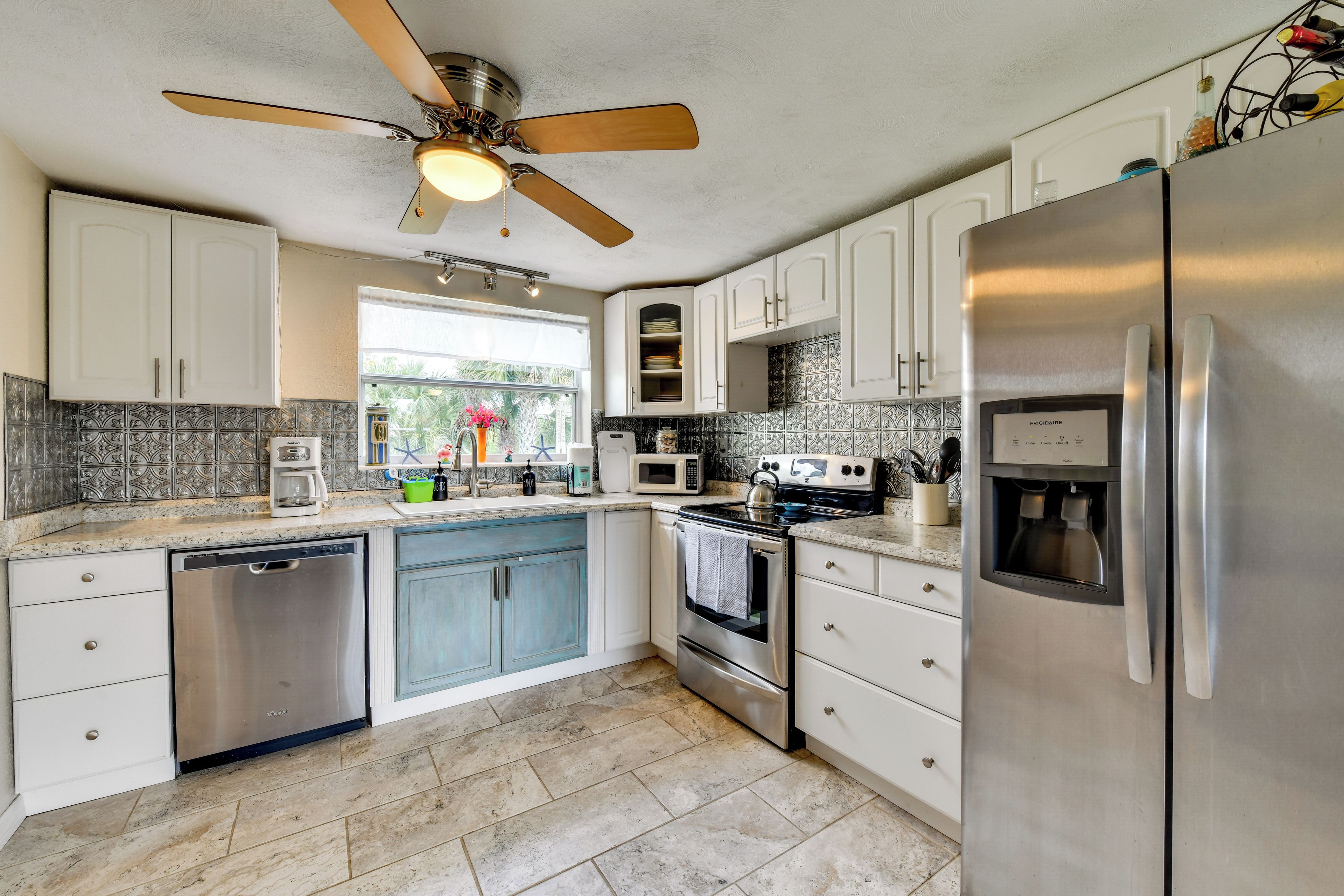 A modern kitchen with white cabinets, stainless steel appliances, and a ceiling fan.