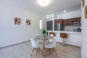 A modern kitchen with a refrigerator, microwave, and a dining area with a glass table and white chairs. - 3 Mi to Beach! Condo w/ Pool in Puerto Morelos (Puerto Morelos)