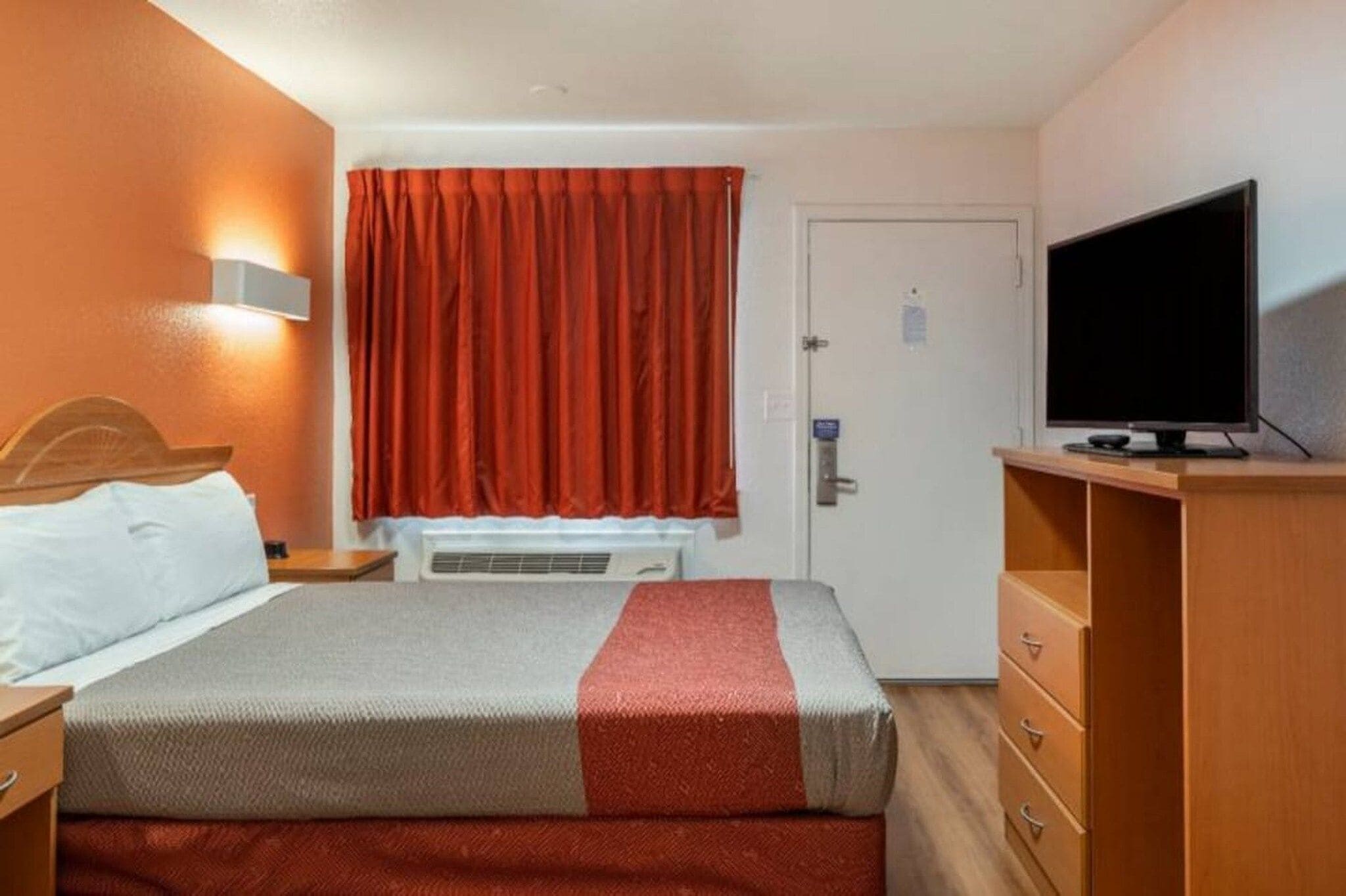 A hotel room with a bed, a television, a wardrobe, and a window with curtains.