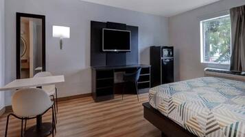 A hotel room with a bed, a desk with a chair, a television, and a wardrobe.