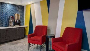 Un vestíbulo de hotel con dos sillones rojos, una cafetera y una recepción con un revestimiento de pared con patrón de espiga.