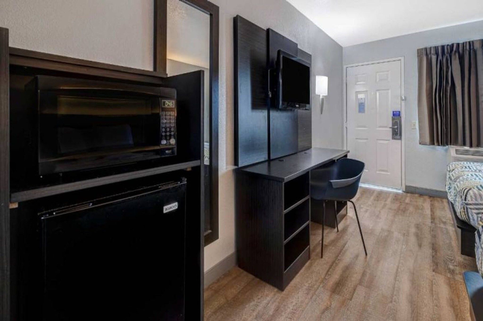 A compact kitchenette with a microwave, a small refrigerator, and a flat-screen TV mounted on the wall.