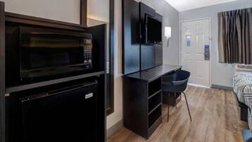A compact kitchenette with a microwave, a small refrigerator, and a flat-screen TV mounted on the wall.