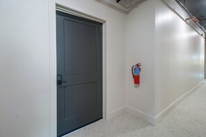 Un couloir avec une porte fermée et un extincteur fixé au mur.