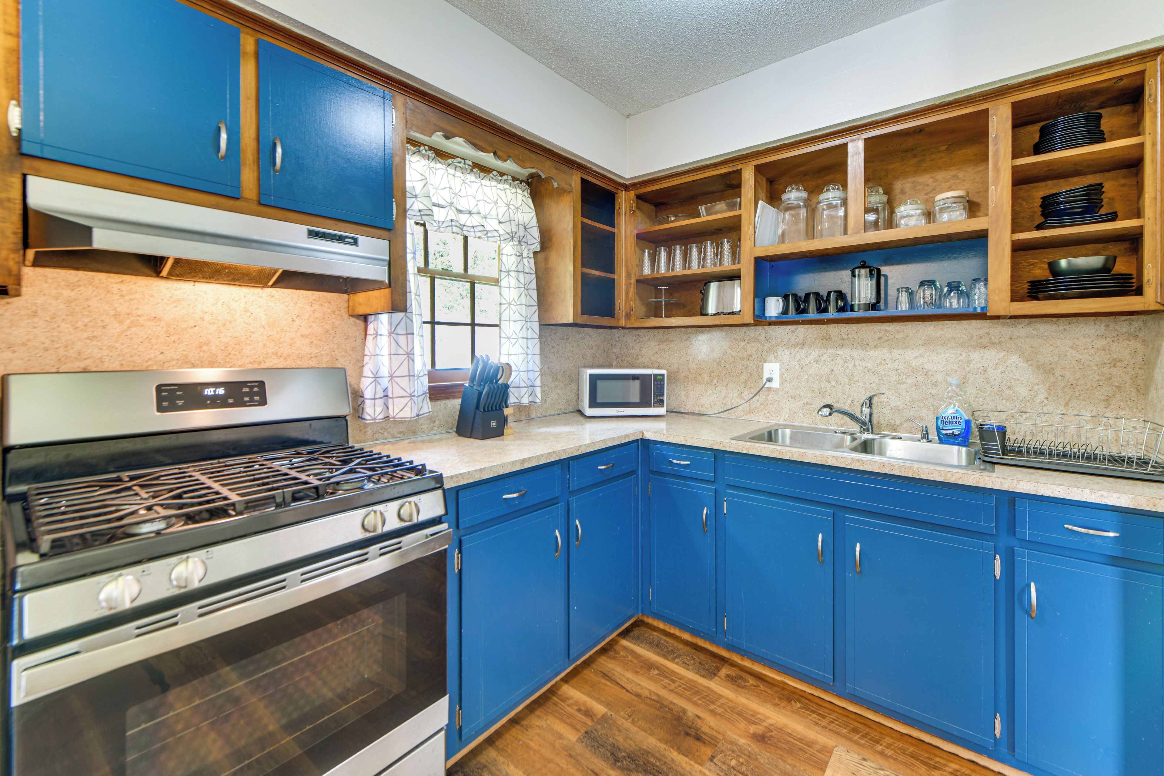 A kitchen with blue cabinets, a stove, a microwave, and a sink.