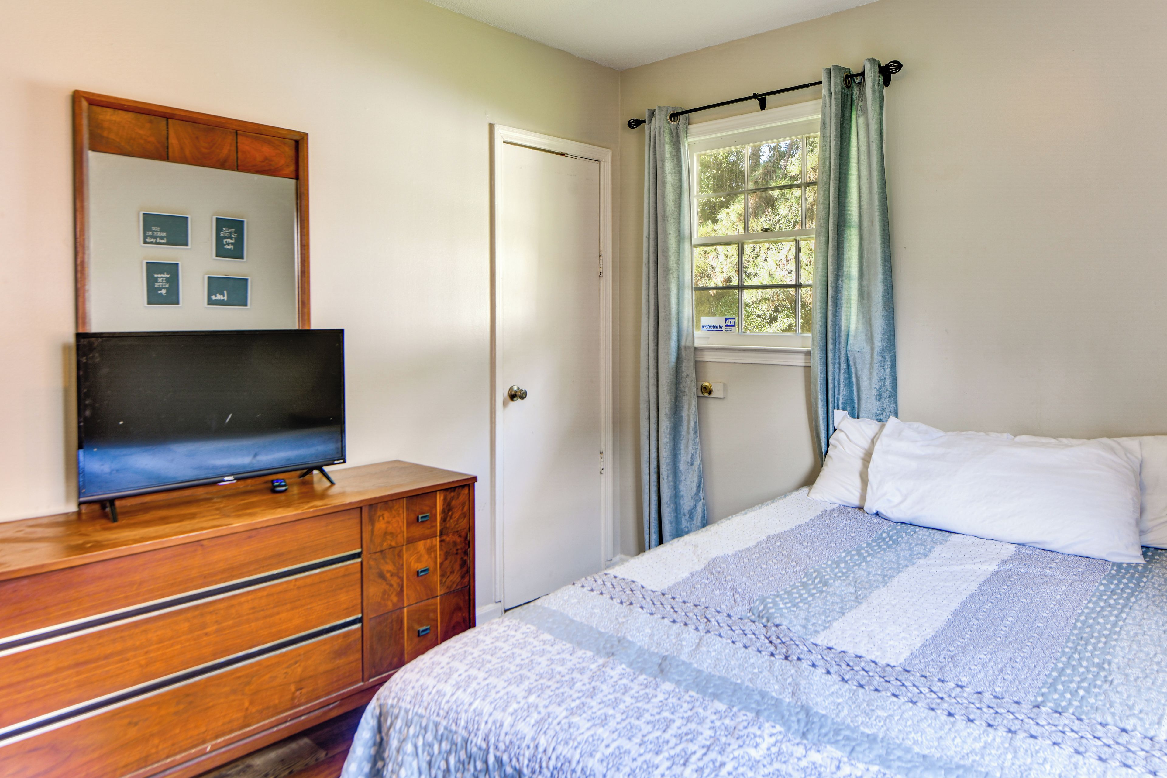 A bedroom with a bed, a dresser, a television, and a window with curtains.