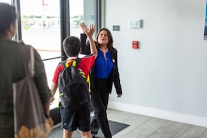 Una mujer con blusa azul y chaqueta negra camina dentro de un edificio con un niño que lleva una chaqueta rojo y negro.