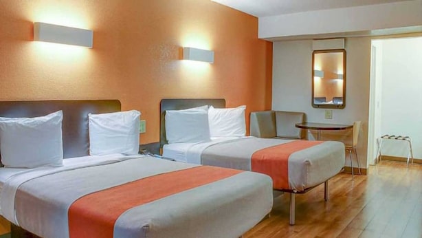 Una habitación de hotel con dos camas, una mesita pequeña y una silla.
