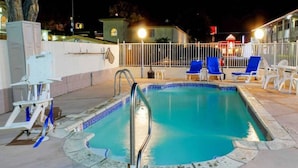Una piscina con una escalera metálica, rodeada por una valla blanca y sillas reclinables azules.