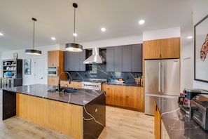 A modern kitchen with a central island, stainless steel appliances, and wooden cabinetry. - Hatcher Pass Northern Lights Home (Palmer)