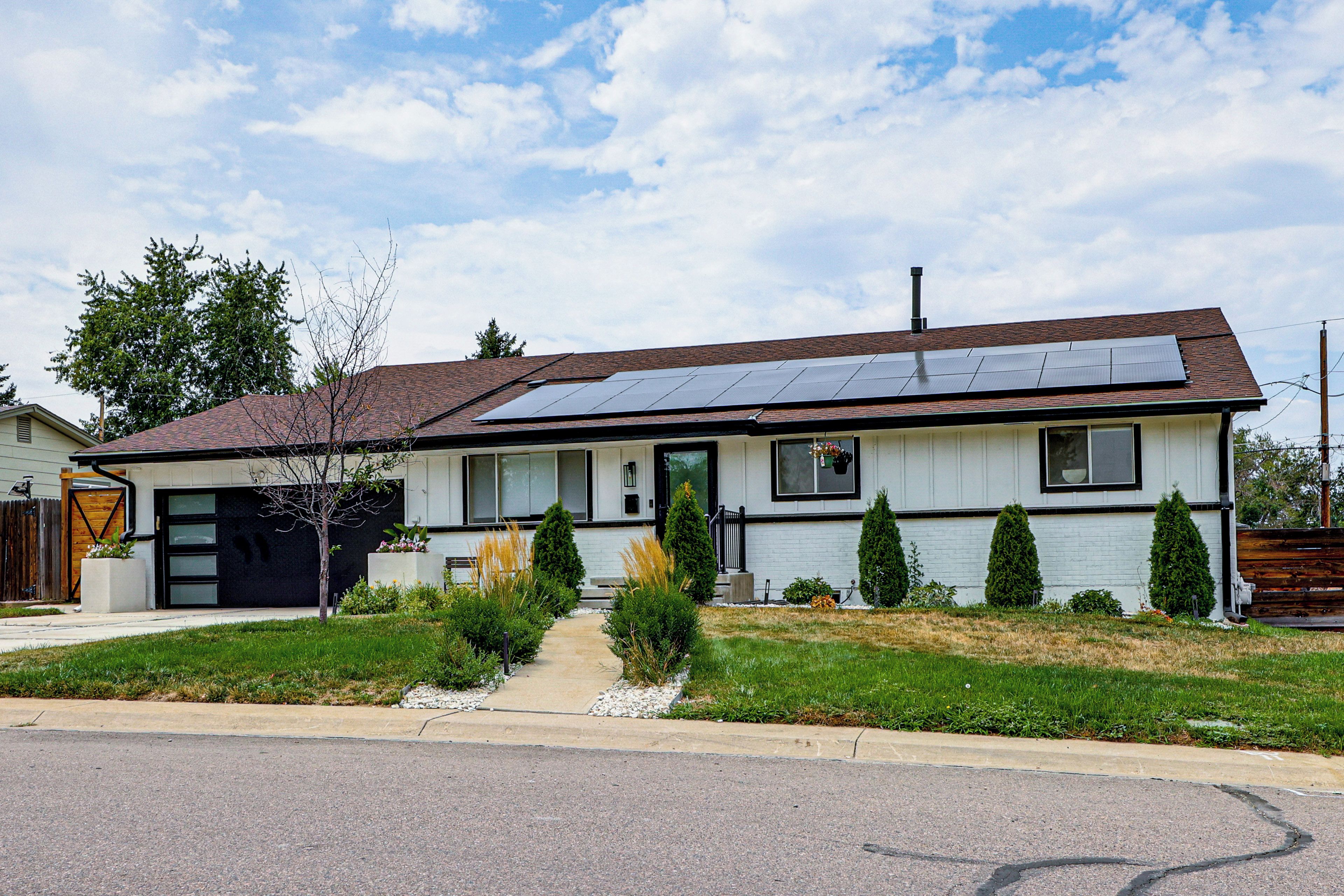 A single-story house with a garage, solar panels, a front yard with a pathway, and a small tree.