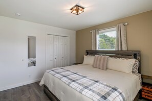 Un dormitorio con cama, ventana con cortinas, puerta y lámpara fijada a la pared.