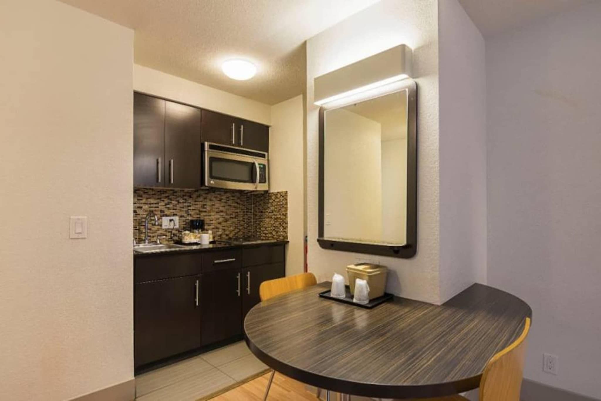 A compact kitchen with dark cabinets, a microwave, and a round dining table with chairs.