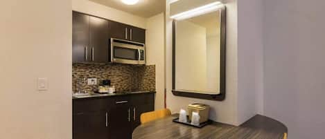 Una cocina compacta con armarios oscuros, un microondas y una mesa redonda con sillas.