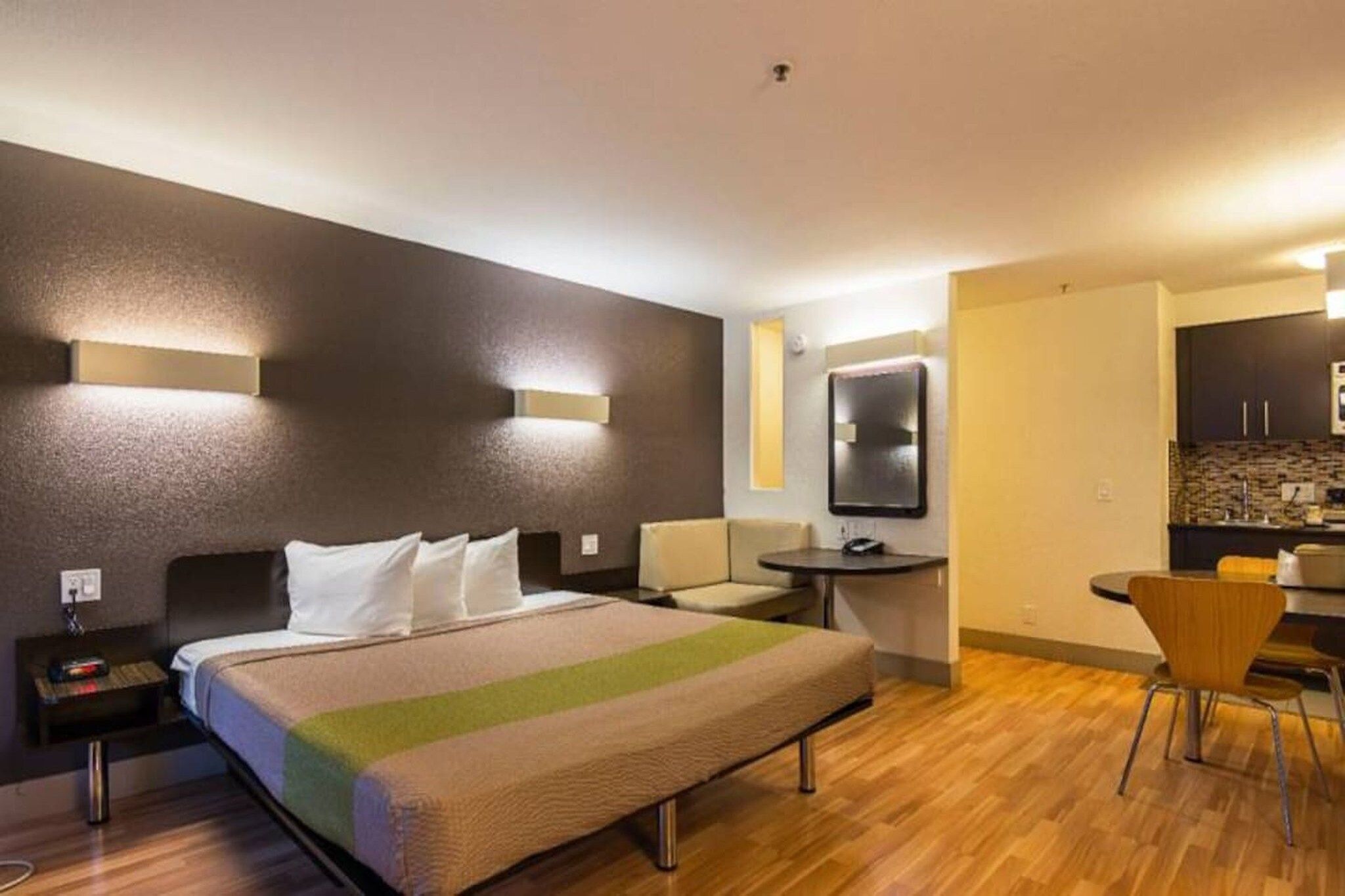 Ein Hotelzimmer mit einem Bett, Nachttischen, einem Schreibtisch, einem Sessel und einer kleinen Küchenzeile.