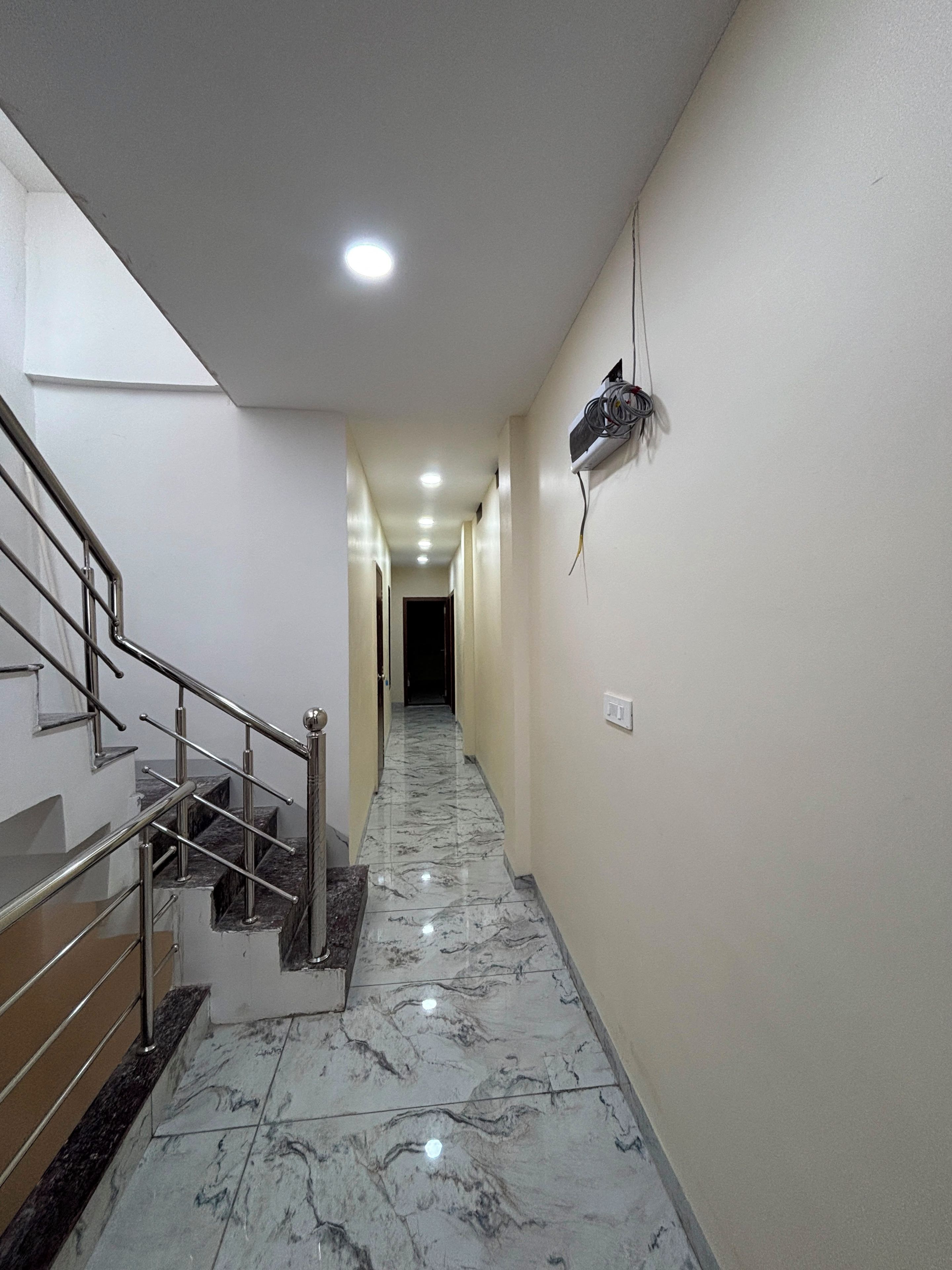 A hallway with a marble floor, a metal staircase, and a wall-mounted electrical box.
