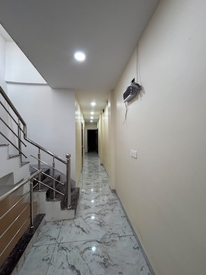 Un pasillo con piso de mármol, una escalera de metal y un cuadro eléctrico en la pared.