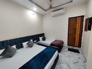 Quarto com duas camas, ventilador de teto, ar condicionado e porta de madeira com cortina estampada.